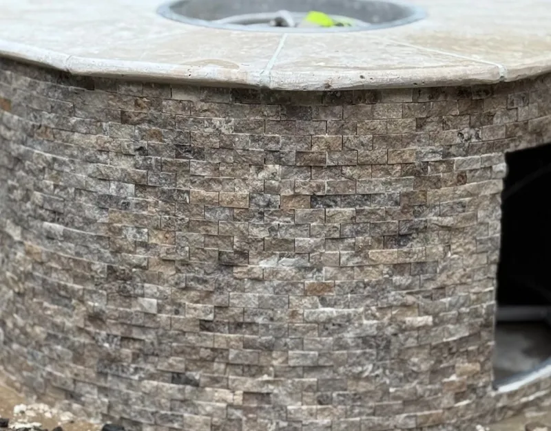 Round fire pit clad in stacked stone with a travertine cap