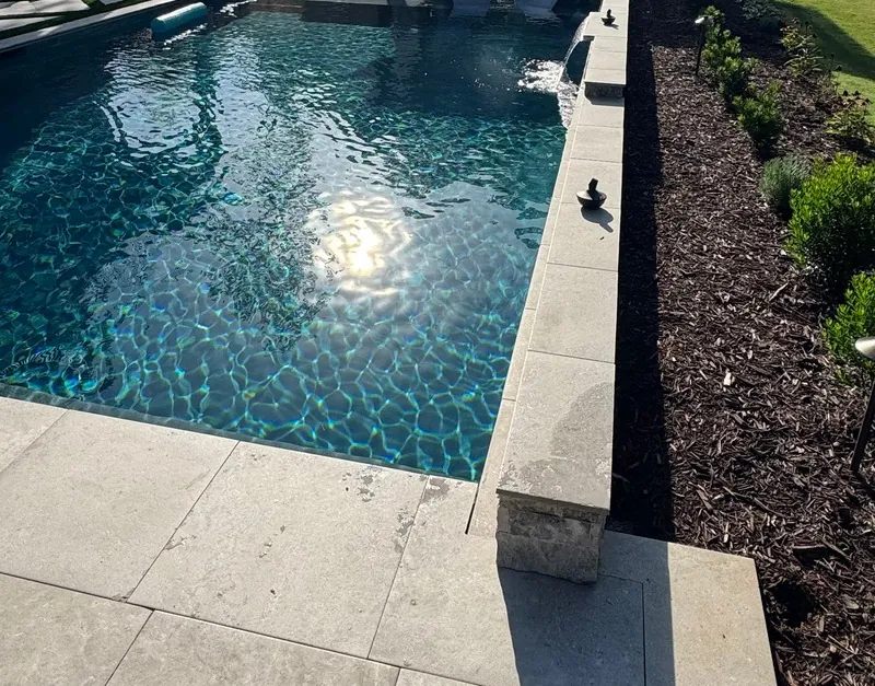 Pool edged in travertine paving beside a planted border